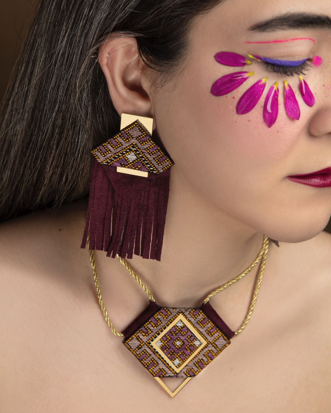 Close-up of a woman wearing a decorative necklace and earrings with floral makeup.