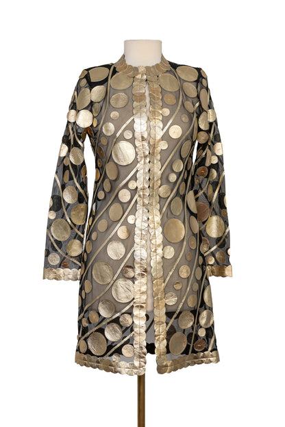Elegant black sheer long-sleeve jacket featuring shimmering gold metallic circular appliqué details, an open-front design with decorative trim, and a lightweight statement silhouette, displayed on a mannequin.